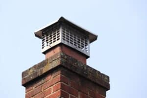 Close-up of a brick chimney with a metal mesh cap against a clear blue sky, showcasing the quality work by a trusted chimney company on Long Island.